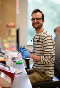 Noah Robinson, promoción de 2021, se sienta en una mesa de laboratorio sosteniendo equipos en Caltech.